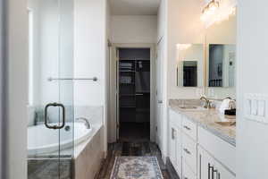 Full bath with double vanity, a bath, wood finished floors, and a stall shower