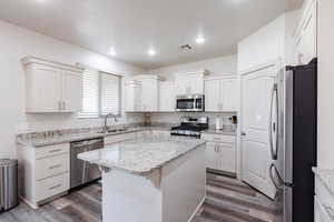 Kitchen featuring appliances with stainless steel finishes, a kitchen island, dark wood-style flooring, white cabinetry, and recessed lighting