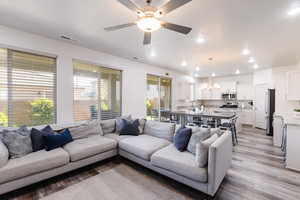Living area with healthy amount of natural light, light wood finished floors, a ceiling fan, a chandelier, and recessed lighting