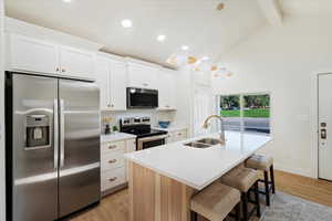 Kitchen with appliances with stainless steel finishes, light wood-style flooring, beam ceiling, a kitchen island with sink, and tasteful backsplash
