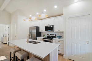 Kitchen with stainless steel appliances, a breakfast bar area, decorative backsplash, light wood finished floors, and a center island with sink