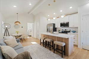 Kitchen with appliances with stainless steel finishes, a kitchen breakfast bar, a center island with sink, decorative backsplash, and white cabinetry