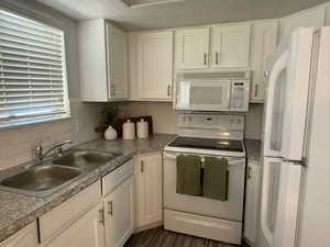 Kitchen with white appliances, a sink, decorative backsplash, white cabinetry, and light countertops