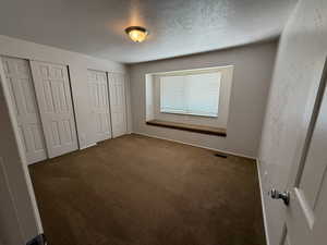 Unfurnished bedroom featuring multiple closets, carpet flooring, a textured ceiling, and baseboards