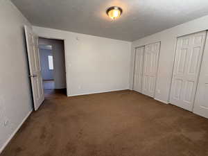 Unfurnished bedroom featuring carpet flooring, baseboards, two closets, and a textured ceiling
