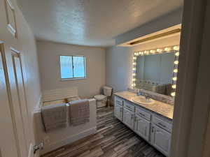 Bathroom featuring toilet, a textured ceiling, vanity, baseboards, and wood finished floors