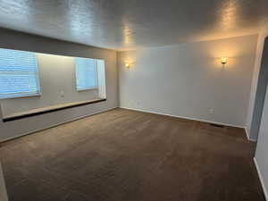 Carpeted empty room with a textured ceiling and baseboards