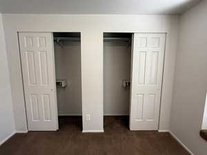 Unfurnished bedroom with dark colored carpet, two closets, and baseboards