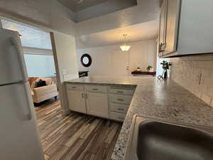 Kitchen with freestanding refrigerator, a peninsula, dark wood-type flooring, decorative backsplash, and a textured ceiling
