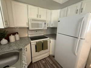 Kitchen with white appliances, dark wood-style floors, white cabinets, a sink, and decorative backsplash