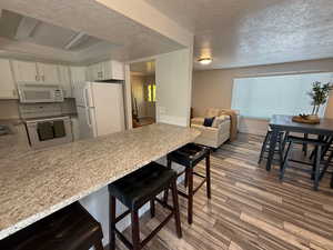 Kitchen with white appliances, a peninsula, wood finished floors, a textured ceiling, and light countertops