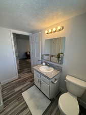 Bathroom featuring vanity, wood finished floors, toilet, a textured ceiling, and baseboards