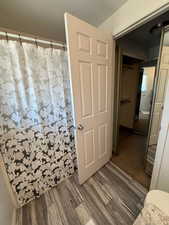 Full bath with curtained shower, toilet, and wood finished floors
