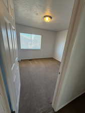 Carpeted empty room with a textured ceiling and baseboards