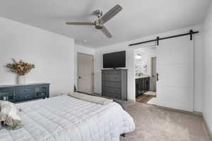 Carpeted bedroom featuring a barn door, ensuite bath, and a ceiling fan