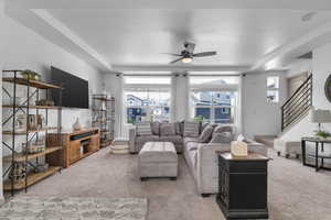 Living room with light colored carpet, healthy amount of natural light, a ceiling fan, a raised ceiling, and a textured ceiling