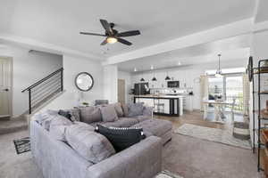 Living area with light colored carpet, a ceiling fan, and stairway