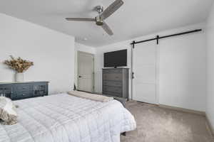 Bedroom featuring a barn door, carpet flooring, and ceiling fan