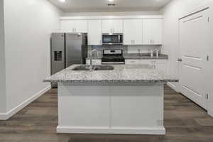 Kitchen with appliances with stainless steel finishes, white cabinetry, an island with sink, and light stone countertops