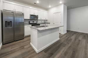 Kitchen with appliances with stainless steel finishes, white cabinetry, a kitchen island with sink, light stone counters, and tasteful backsplash