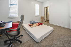 Carpeted bedroom featuring multiple windows, a desk, and ensuite bath