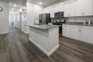 Kitchen featuring appliances with stainless steel finishes, an island with sink, dark wood finished floors, white cabinets, and decorative backsplash