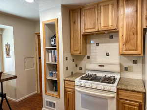 Kitchen with white gas range, decorative backsplash, wood finished floors, light stone countertops, and a textured ceiling