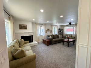 Carpeted living room featuring recessed lighting, healthy amount of natural light, a stone fireplace, and a ceiling fan