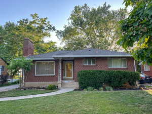 Ranch-style home with brick siding, a front yard, a chimney, and a shingled roof