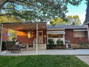Rear view of house featuring brick siding, a patio area, and a shingled roof