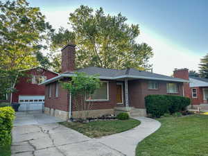 Ranch-style home with a chimney, a detached garage, an outdoor structure, a front lawn, and brick siding
