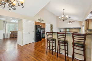 Kitchen featuring black appliances, a chandelier, vaulted ceiling, dark wood finished floors, and dark countertops