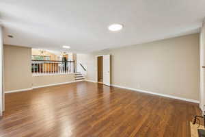 Empty room featuring a chandelier, wood finished floors, stairs, and a textured ceiling