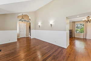 Unfurnished room with a chandelier, wood finished floors, and high vaulted ceiling