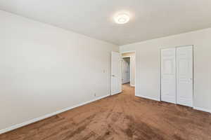 Unfurnished bedroom with light colored carpet, a closet, and a textured ceiling
