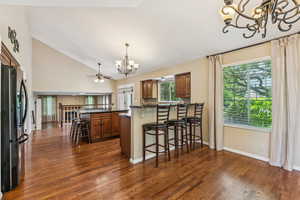Kitchen with a chandelier, refrigerator with ice dispenser, brown cabinetry, dark countertops, and lofted ceiling
