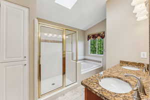 Full bath featuring lofted ceiling, a garden tub, a shower stall, a skylight, and double vanity