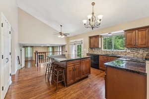 Kitchen with black dishwasher, backsplash, dark wood-style flooring, a chandelier, and a kitchen breakfast bar