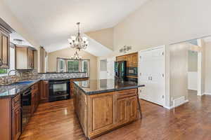 Kitchen with black appliances, a chandelier, vaulted ceiling, decorative backsplash, and brown cabinets