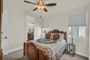 Carpeted bedroom featuring ensuite bath and a ceiling fan
