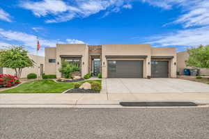 Southwest-style home featuring stucco siding, an attached garage, driveway, stone siding, and a front yard