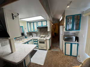Kitchen featuring white appliances, under cabinet range hood, light countertops, backsplash, and carpet flooring
