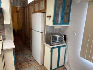 Kitchen featuring freestanding refrigerator, backsplash, light countertops, and glass insert cabinets