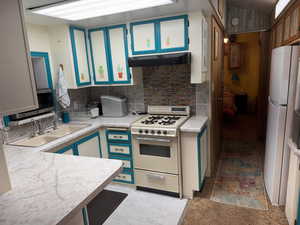 Kitchen with gas range oven, freestanding refrigerator, light countertops, backsplash, and stainless steel microwave