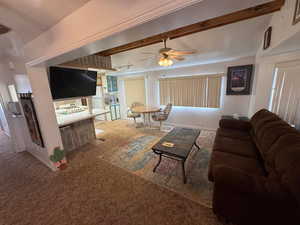 Carpeted living room with ceiling fan and beamed ceiling