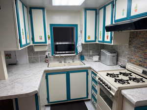 Kitchen with white gas range oven, stainless steel microwave, light countertops, decorative backsplash, and blue cabinets