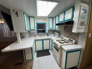 Kitchen with white range with gas cooktop, under cabinet range hood, light countertops, stainless steel microwave, and backsplash