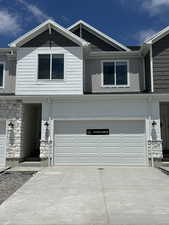Townhome / multi-family property with a garage, stone siding, driveway, and board and batten siding