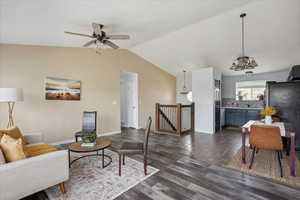 Living room with vaulted ceiling, ceiling fan, dark wood finished floors, and a chandelier