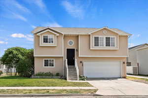 Raised ranch featuring stucco siding, a garage, and driveway